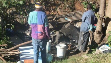 Two displaced people stand next to their 'household' utensils placed in their street 'shelter'. Photo: Naidine Sibanda