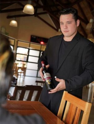 Third-year student at the IIE School of Hospitality and Service Management Daniël de Bruin serves a bottle of wine to a client.