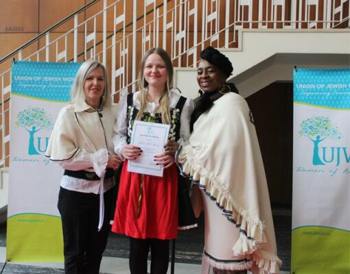 UJW sewing school manager Ariane Heneck and teacher Nomvula Siduge present a graduation certificate to Anouk Heneck on June 18, 2026. Photo: Thato Modopi