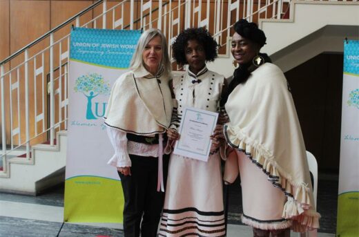 UJW sewing school manager Ariane Heneck and teacher Nomvula Siduge present a graduation certificate to Thelma Sikazwe on June 18, 2026. Photo: Thato Modopi