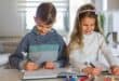 Two children drawing in notebooks at a table.