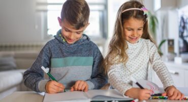 Two children drawing in notebooks at a table.