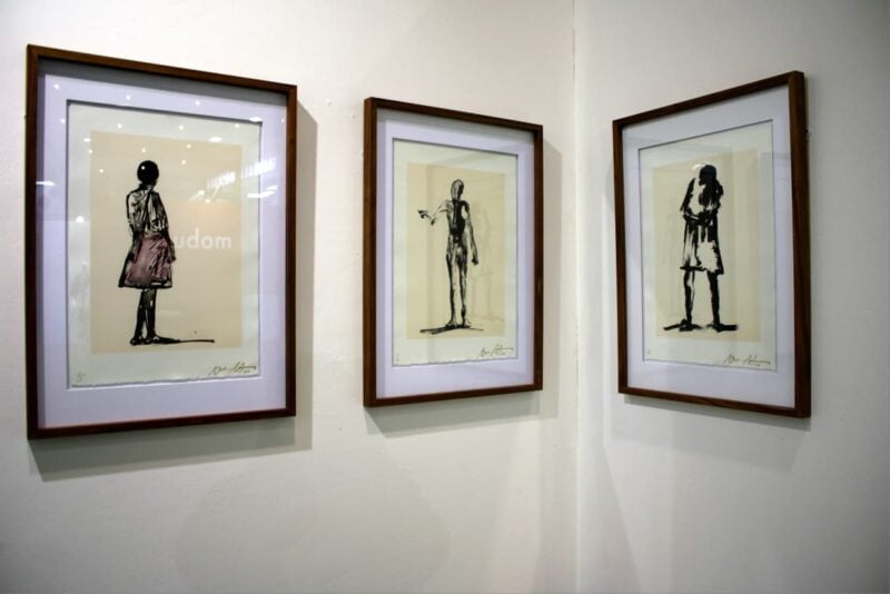 Three limited-edition prints hang side by side in matching wooden frames, each showing a lone standing figure in loose, gestural black ink on a warm cream ground in Houghton on October 1, 2026. Photo: Naziya Davids-Easthorpe