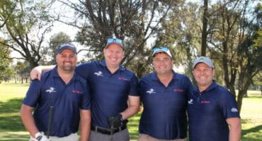 Manne staan met golfstokke in hulle hande op golfbaan.