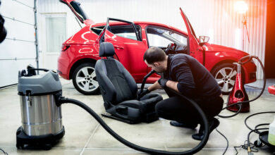 Car service worker cleaning car seat with vacuum cleaner.
