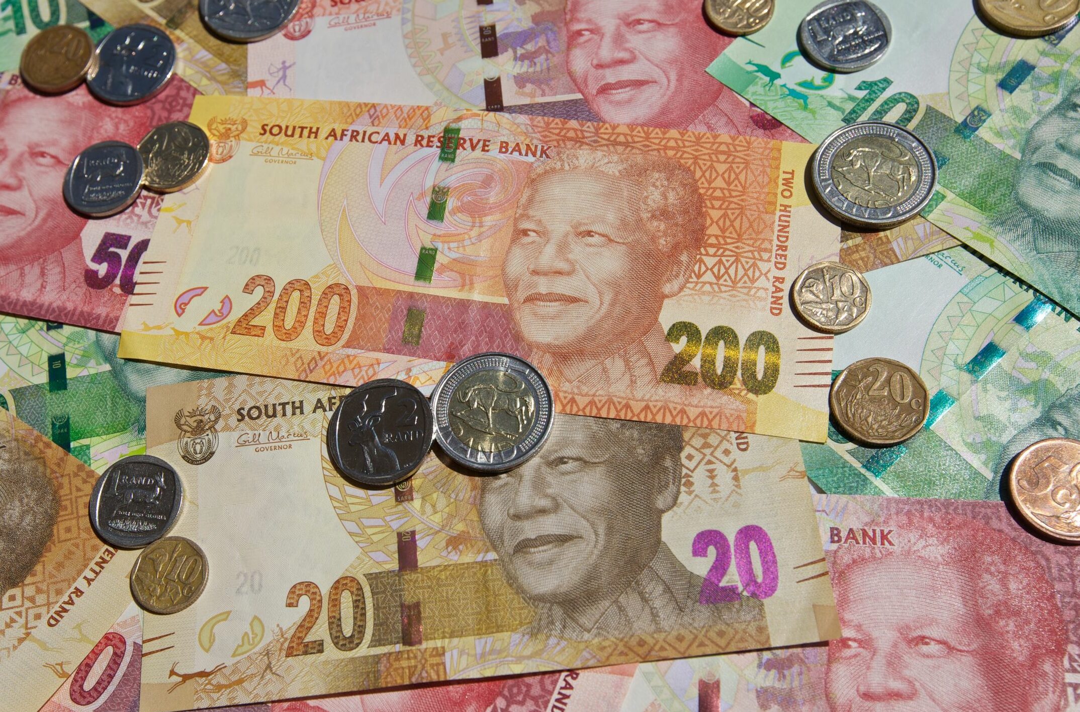 South African rand banknotes and coins scattered, symbolising financial news and currency exchange.