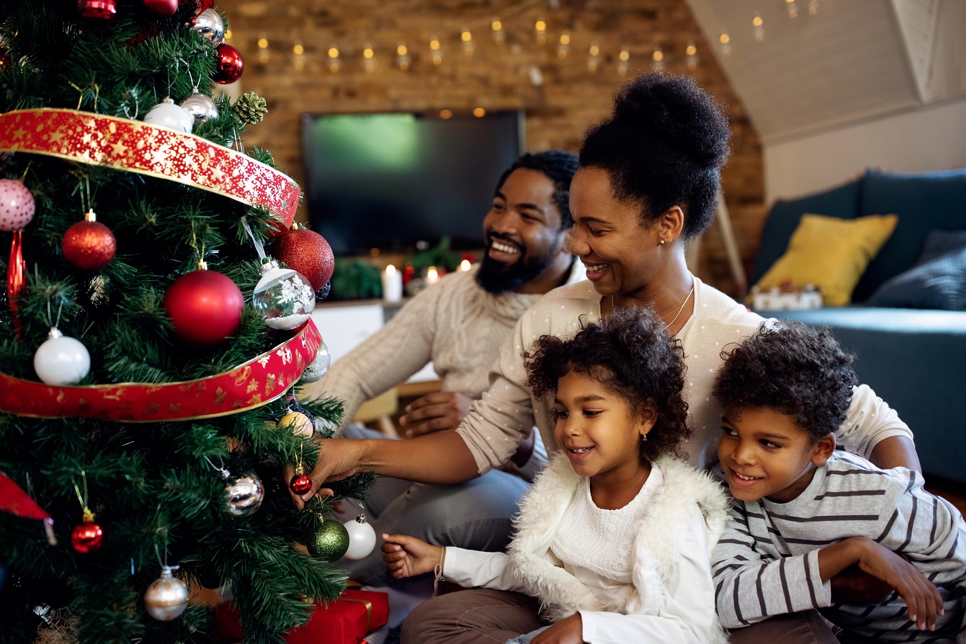Happy African American family decorating Christmas tree at home.