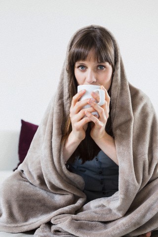 Portrait of mid adult woman covered with blanket and holding cup of tee