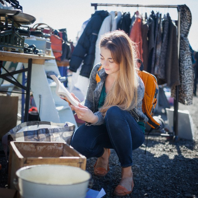 Young woman on flea market looking through displayed products