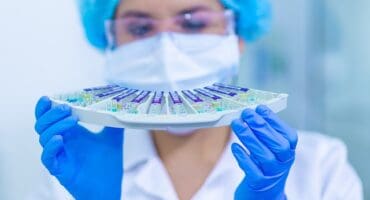 woman wearing a mask in laboratory looking at test tubes