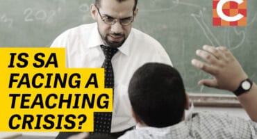 A teacher in a classroom, standing in front of a pupil. Image text reads: Is SA facing a teaching crisis?