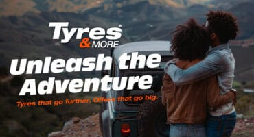 A man and woman embracing while looking over their 4x4 vehicle to the scenery below.