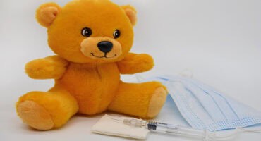 Tan teddy bear with a syringe and medical mask