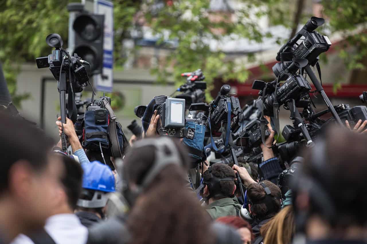 professional video cameras, many mounted on tripods, to capture an event. The cameras and the backs of people's heads dominate the foreground, suggesting a focus on media coverage or a public gathering of significant interest.