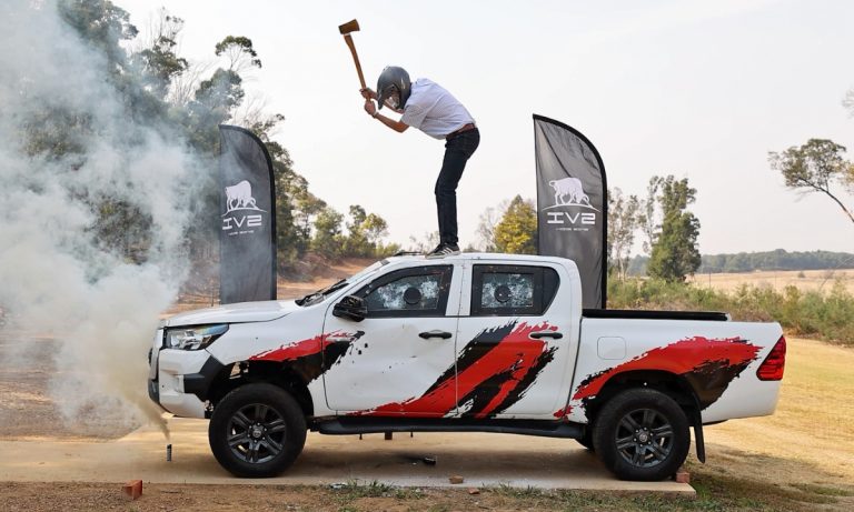 Man with a hammer wearing a helmet standing on the roof of a Toyota Hilux double cab bakkie