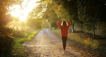 A person walks alone down a peaceful tree-lined path at sunrise, symbolising self-care, reflection and mental wellbeing for caregivers and therapists.