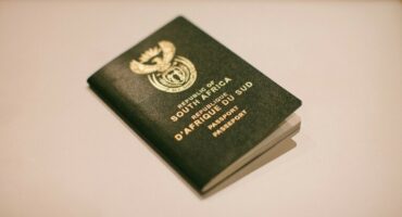 A South African passport lies closed on a light surface. Its green cover features the national emblem and text in English and French, denoting a formal and official appearance.