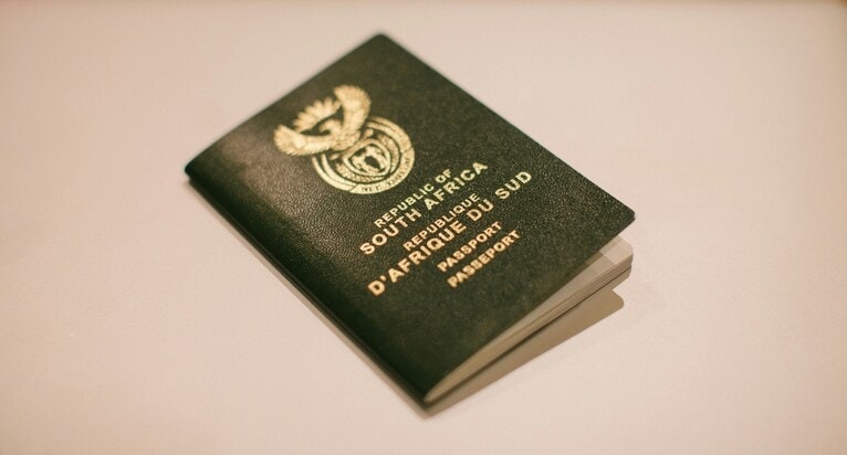 A South African passport lies closed on a light surface. Its green cover features the national emblem and text in English and French, denoting a formal and official appearance.