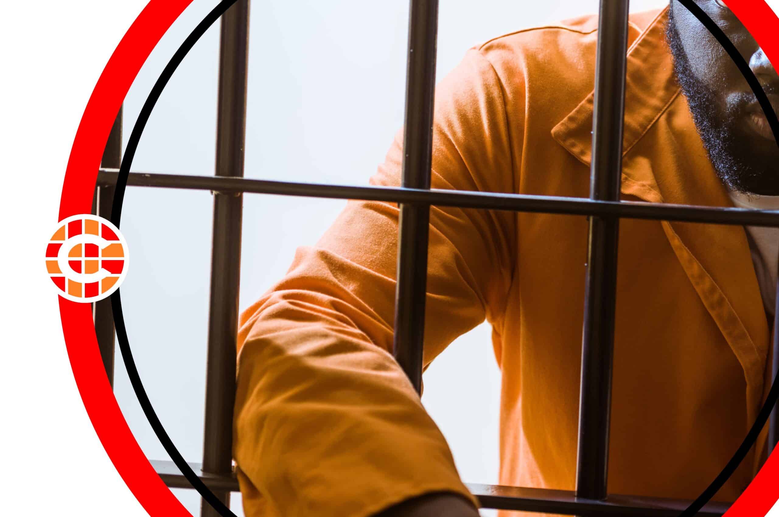 A man in an orange jumpsuit, leaning against bars in a jail cell.
