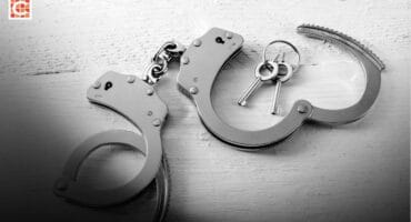 A pair of silver-coloured handcuffs laying on a white surface.