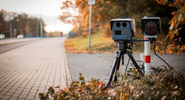 Photo of a speed camera behind some bushes next to a road.