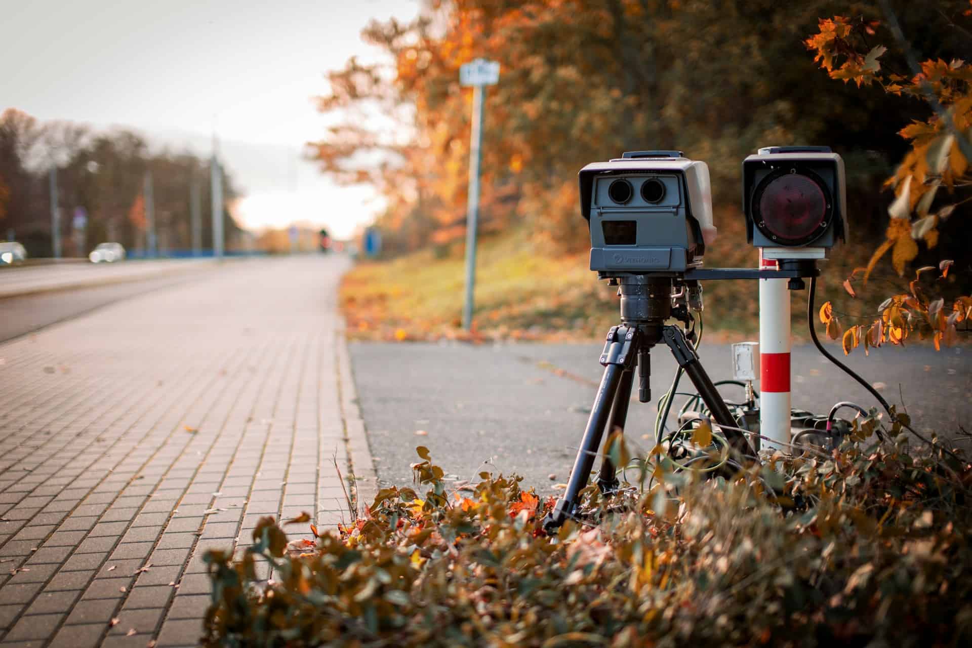 Photo of a speed camera behind some bushes next to a road.