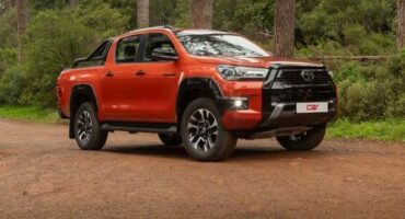 side view of a burnt orange toyota hilux double cab bakkie with a forest in the background.