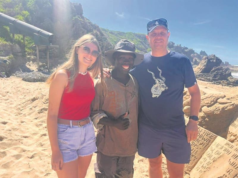 Three people standing on a beach next to a sand sculpture
