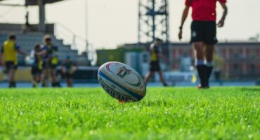 A rugby ball set up for a kick with a referee walking towards it in the background.