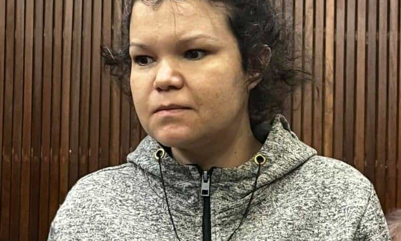 Head and shoulders photo of woman with dark hair and grey hoodie standing before a wooden-panelled wall