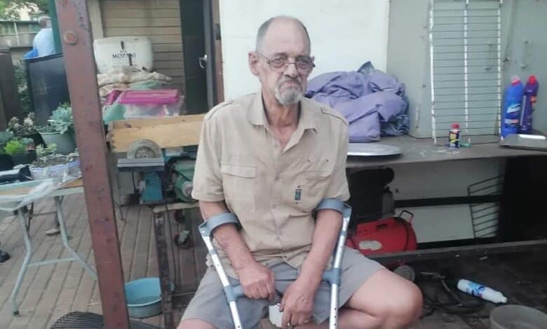 Man with crutches dressed in a khaki shirt sitting on a chair.