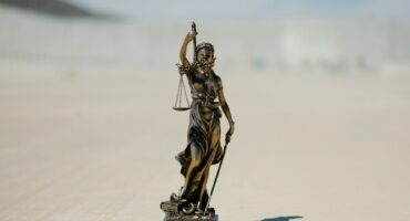 Bronze sculpture of lady justice on a sandy coloured background.