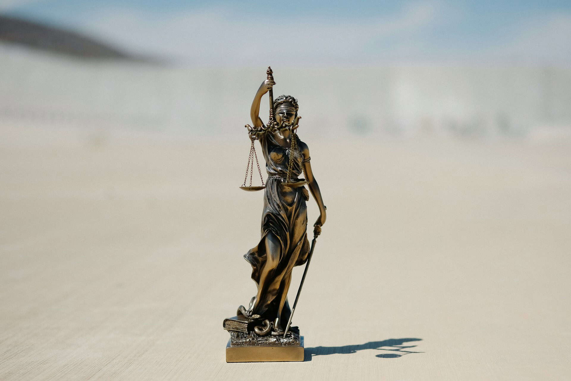 Bronze sculpture of lady justice on a sandy coloured background.