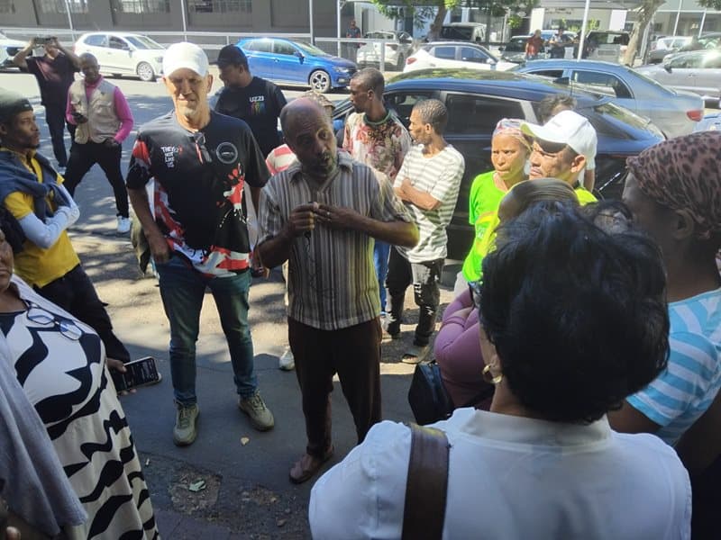 People standing outside a court building with cars parked in the background