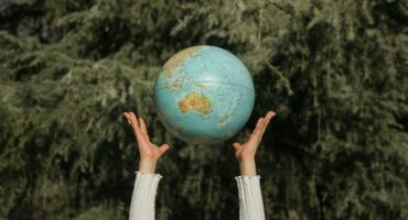Hands throwing a soccer ball-sized earth globe into the air with tree branches visible in the background
