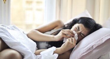 woman lying on bed blowing her nose