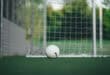 White soccer ball lying on a green pitch in front of a white goalpoast
