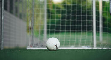 White soccer ball lying on a green pitch in front of a white goalpoast