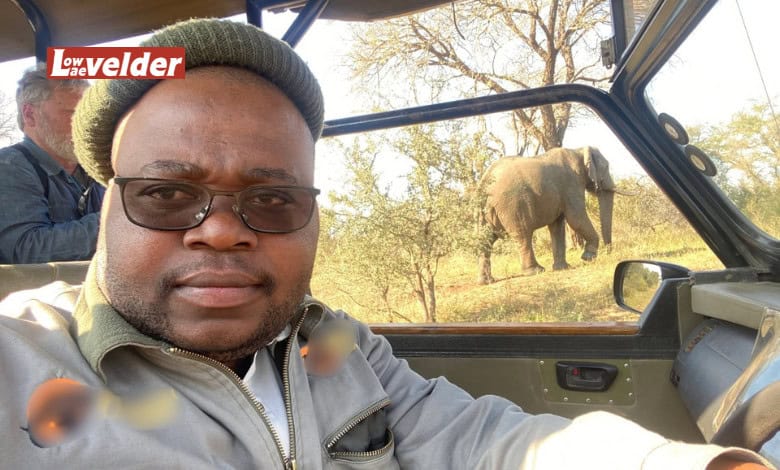 Tour guide wearing glasses in a game viewing vehicle with an elephant visible over this left shoulder.
