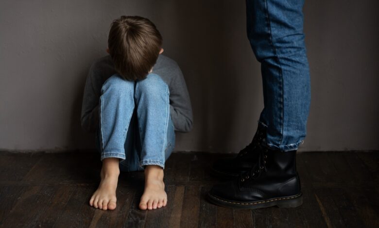Young boy sitting on a floor with his head on his knees and adult legs visible to his right.