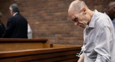 Bald man in court, appearing distressed and looking down.
