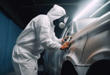 Car painter in protective clothes paints automobile with paint in chamber workshop. Generative AI