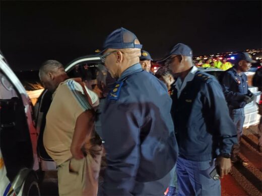 A group of police officers in uniform gather around a man in a beige outfit during a police operation.