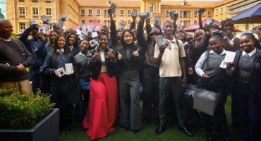 Students celebrate while holding newly received smartphones during a school handover event.