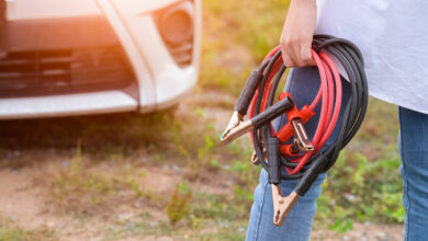 Closeup of woman hand holding battery cable copper wire for repairing broken car by connect battery with red and black line to electric terminal by herself. Car maintenance and transportation concept