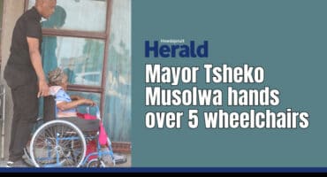 Mayor Tsheko Musolwa pushes an elderly woman in a wheelchair.