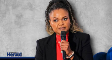 Mandla Mabunda holds a microphone with a grey background.