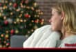 A woman sits alone with Christmas decorations in the background.