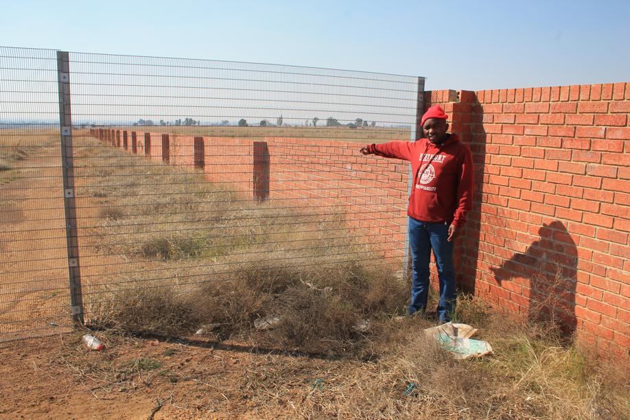 Mr Sbu Ndubata shows the partially built section of the wall beyond the fence that is puzzling residents.