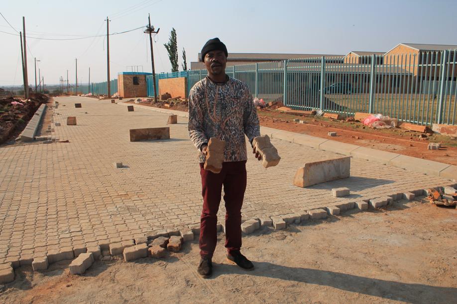 Mr Chucku Kerileng shows, on the left, one of the bricks that have bene taken out of the road. On the right is one of the bricks tha are now being laid.
